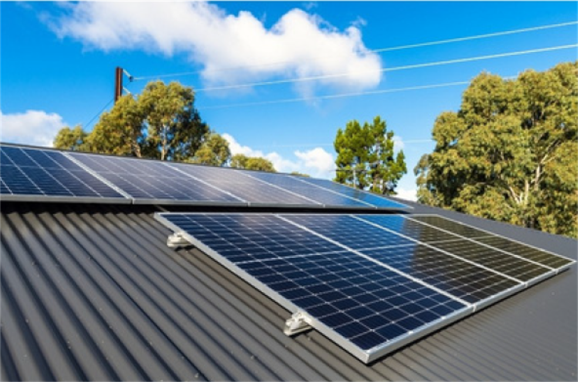 Solar panels on a grey rooftop with a sunny sky in the background