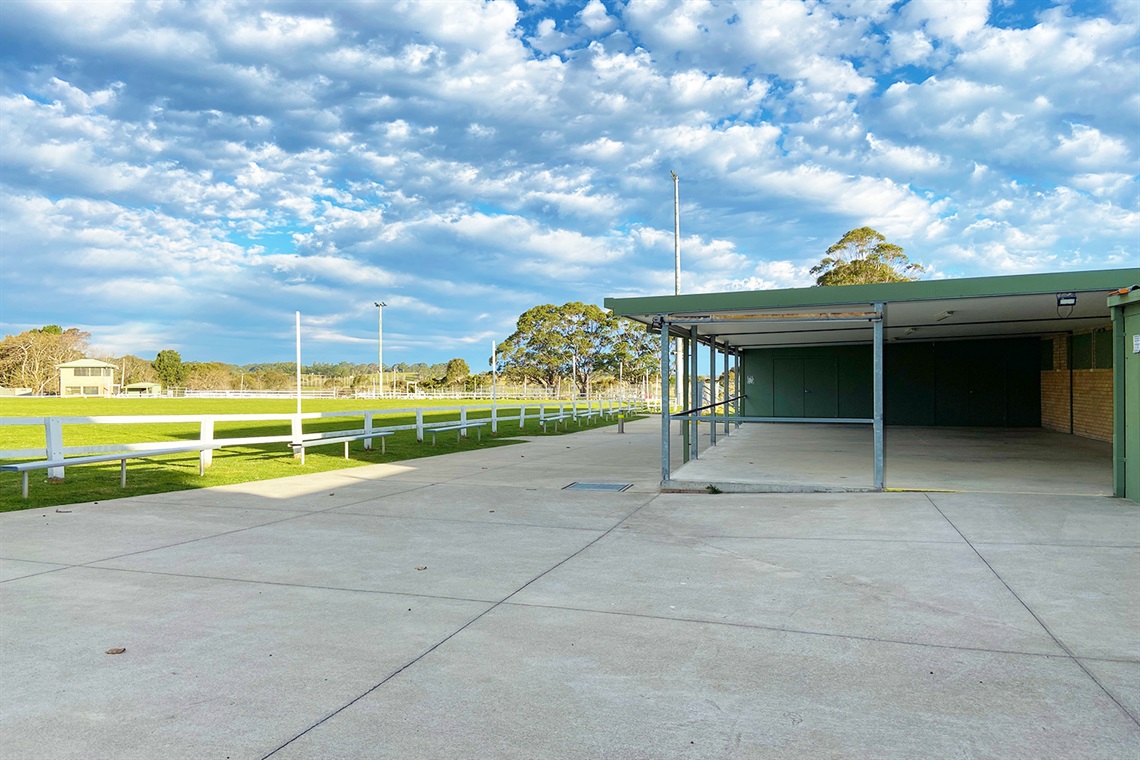 The exterior view of the outdoor dining area of the showground kitchen. There's an open concrete space surrounding the covered dining area, and the main arena is visible to the left.