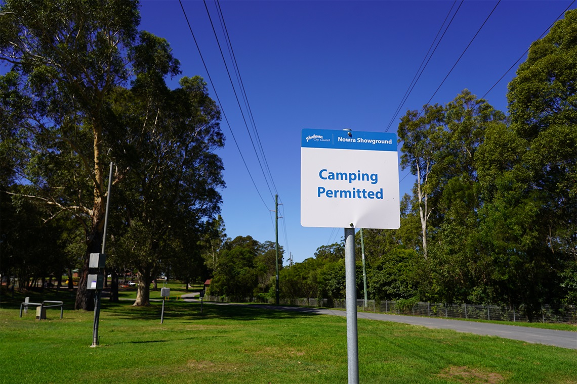 Sign for Nowra Showground Campgound with powered sites, corridors of trees and sealed showground roadway. 