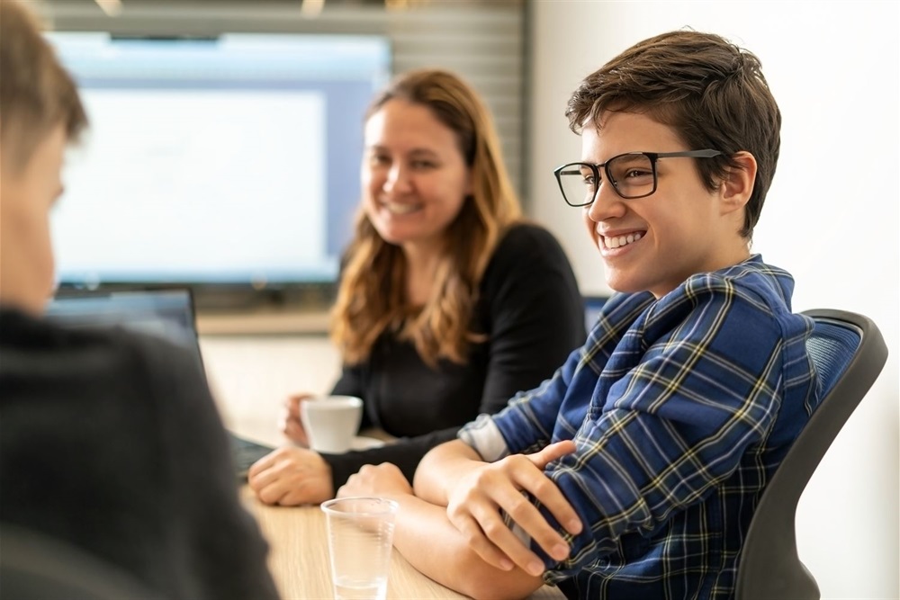 A young person with glasses talking to colleagues in the office