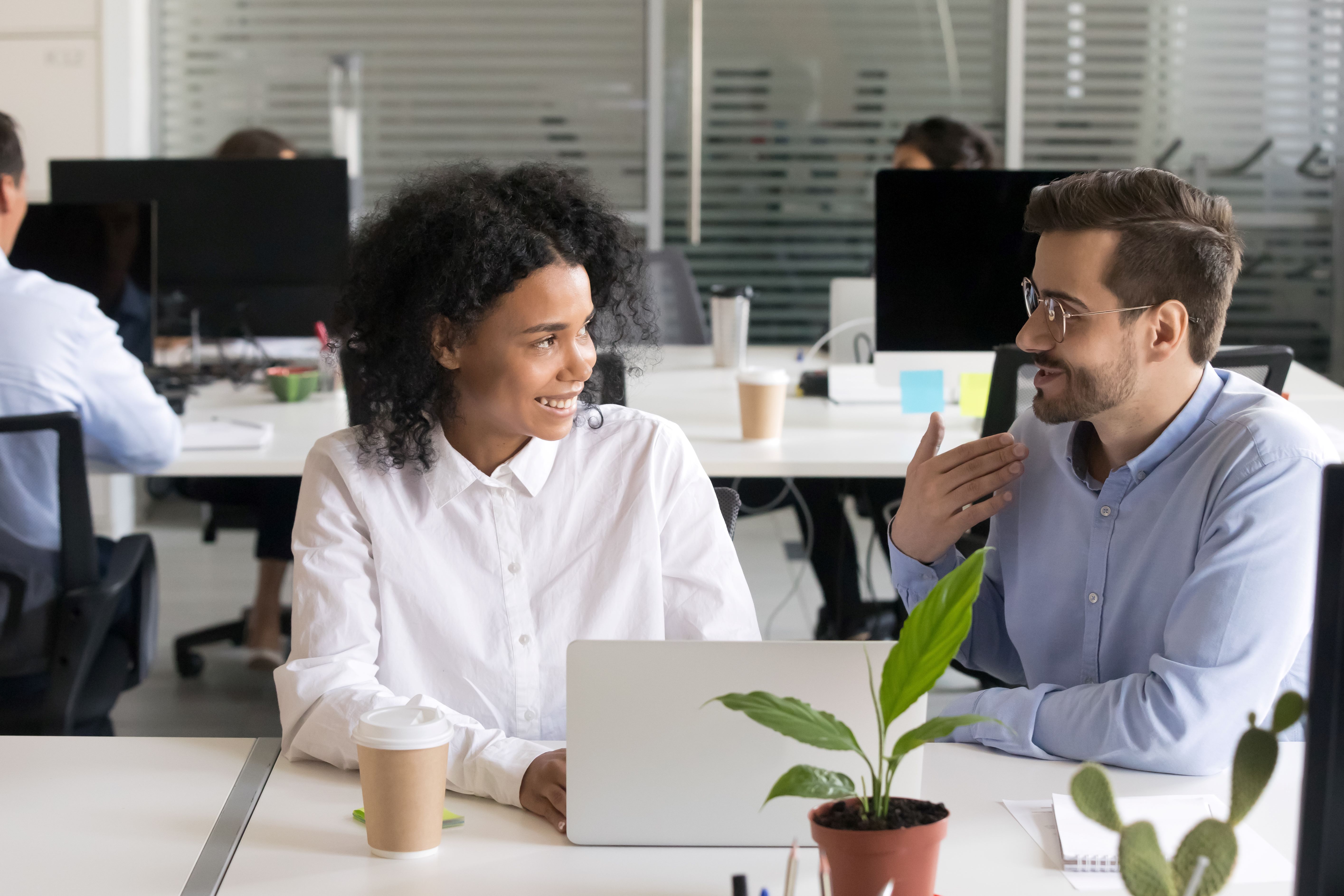 Two young people having a conversation at a desk in an office