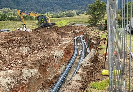 A photo of pipes in a trench with an excavator in the background.