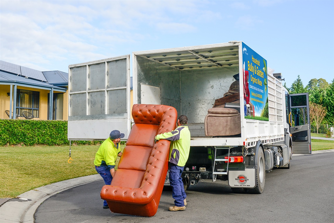 Workers loading a three seater couch into a bulky waste truck