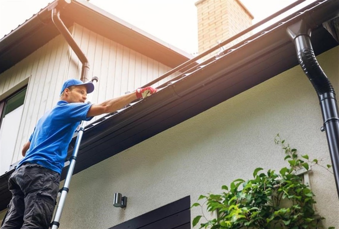 Person on step ladder cleaning leaves from gutter