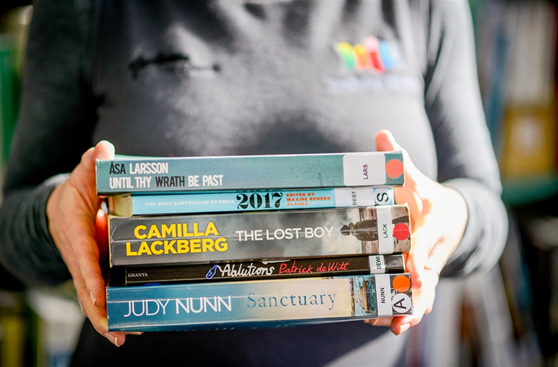 Close up of Shoalhaven Library employee holding five assorted book titles