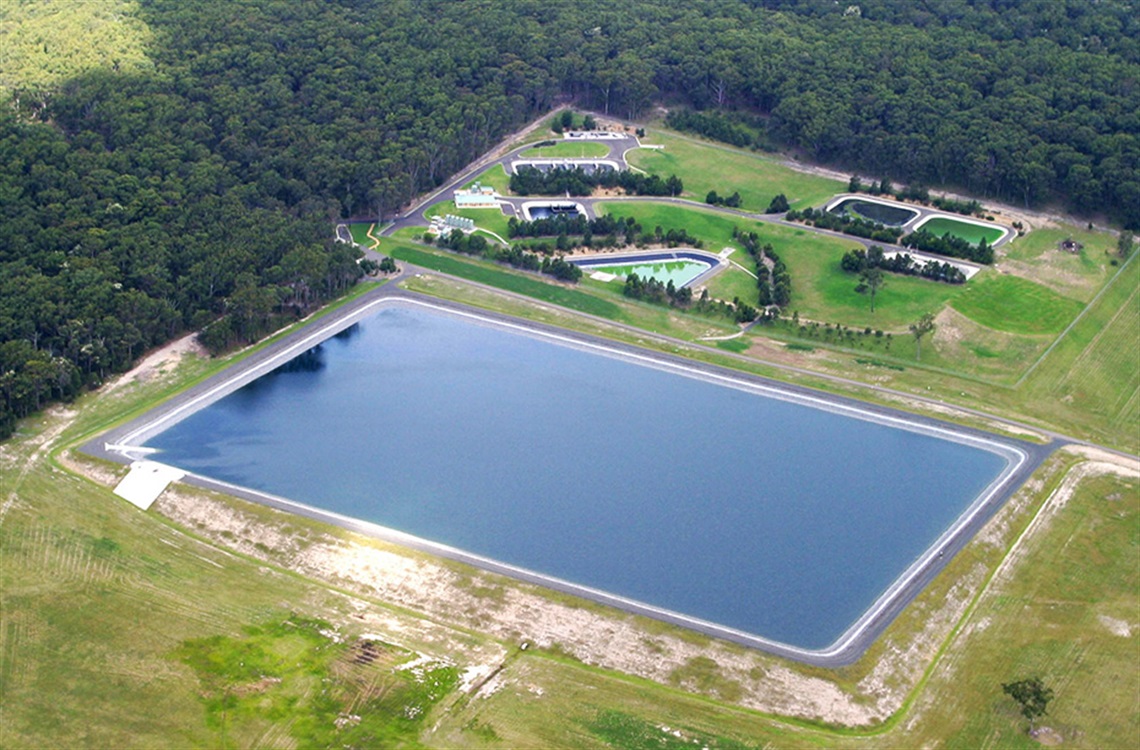 Aerial view of large rectangular water treatment pond surrounded by grass and bushland