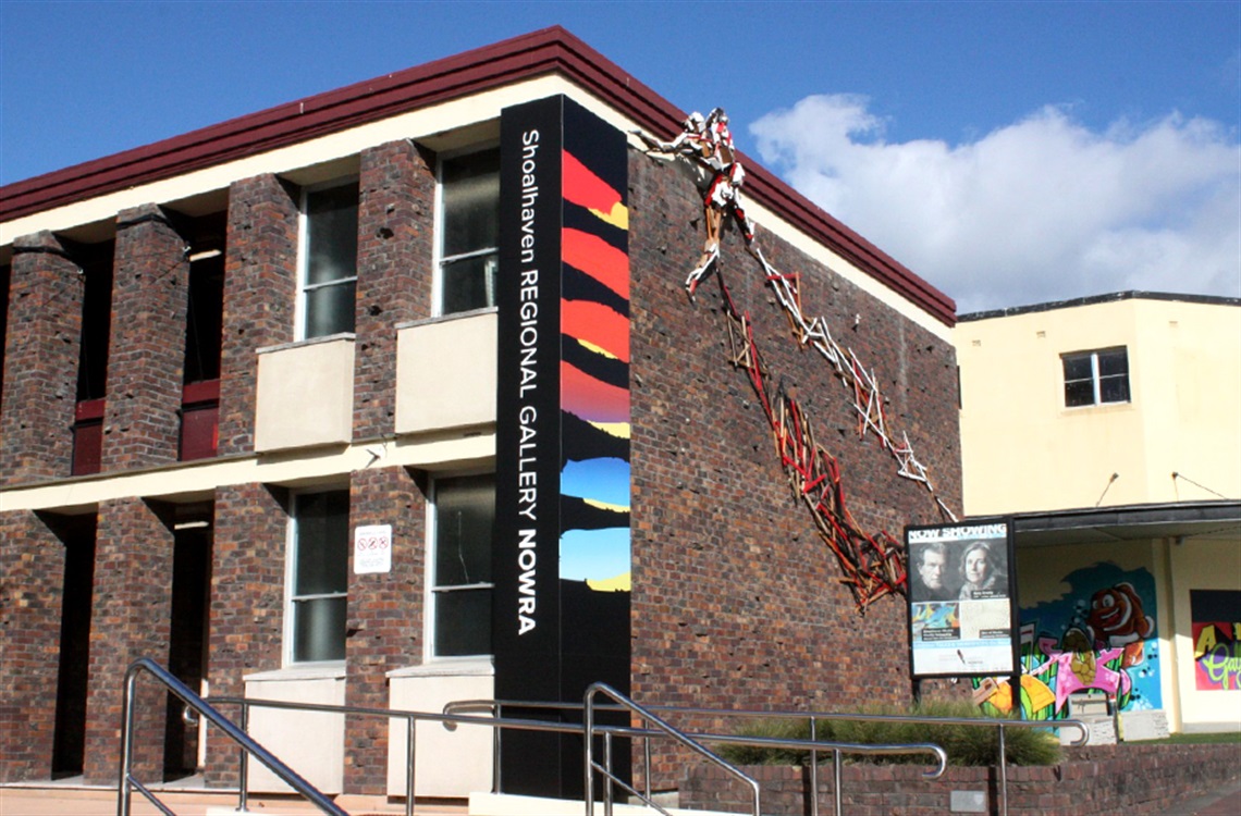 Street view of two storey brick building with art installation on wall and large format signage