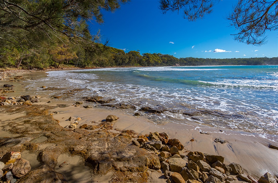 Beach with rocky shore and gentle waves surrounded by bushland