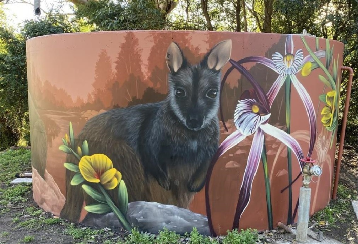 A photo of a water storage tank with a painted mural of Australian native plants and animals