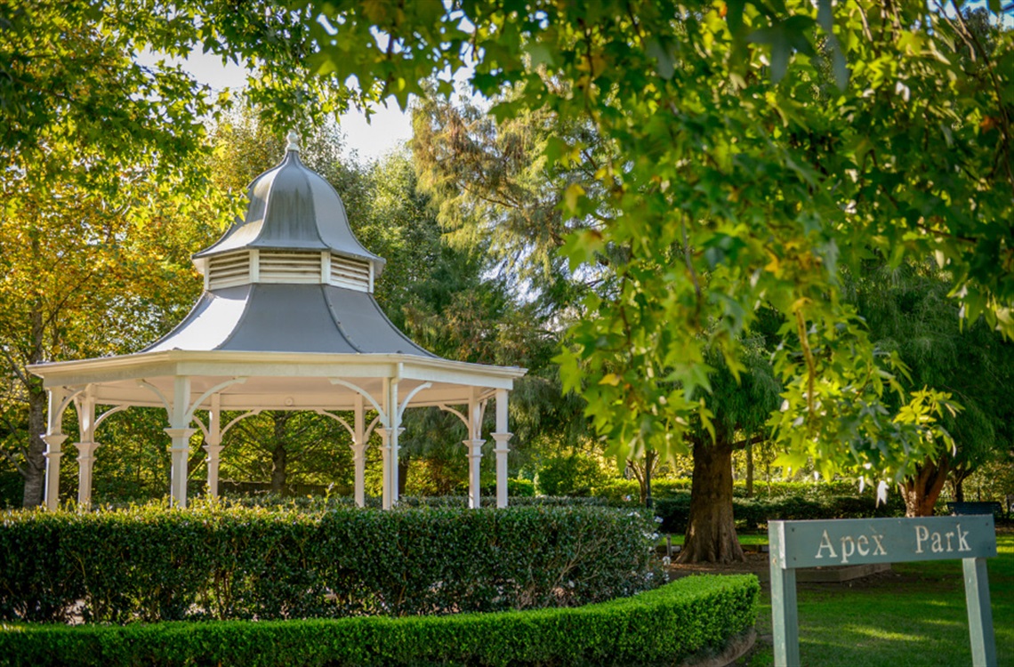 A circular gazebo surrounded by a box hedge and trees in park