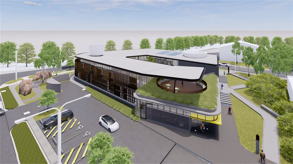 An architectural render of the planned Sanctuary Point Library. It shows computer graphics of a modern-looking library building with a grass roof section and surrounding gardens and pathways, with a small car park in front.