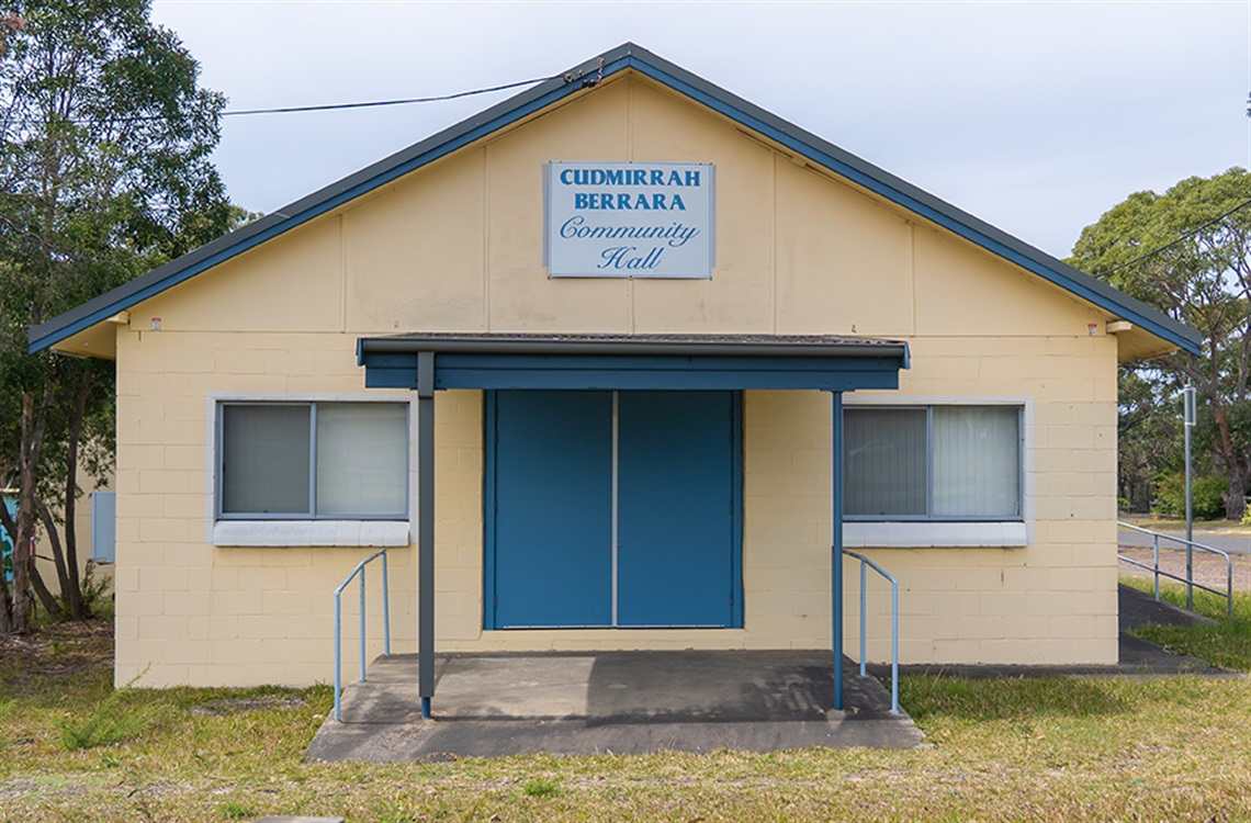 Street view of yellow community hall with pitched roof and double door entrance