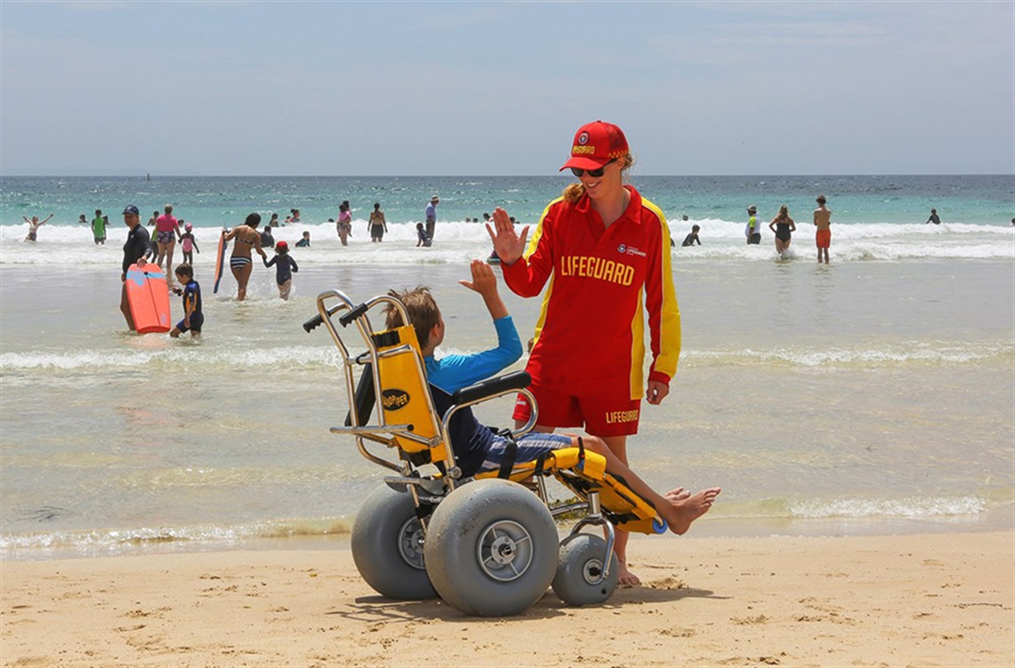 Child in beach wheelchair high-fiving lifeguard
