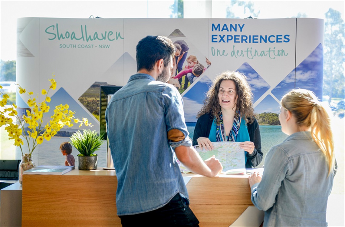 Shoalhaven Tourism employee giving directions on a map to young couple from information booth