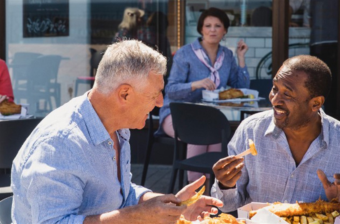 Two men enjoying fish and chips outdoors sitting at table