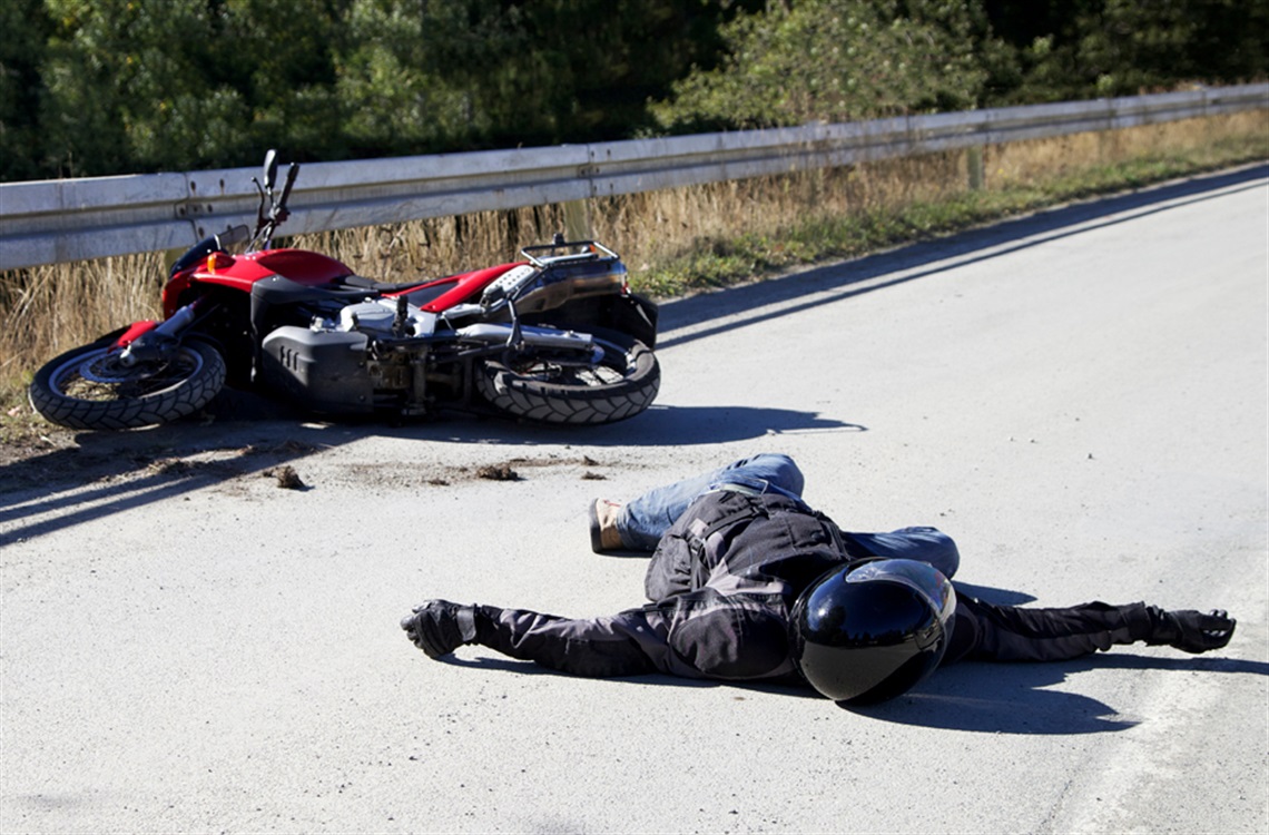 Motorcycle rider laying on road with bike crashed in background