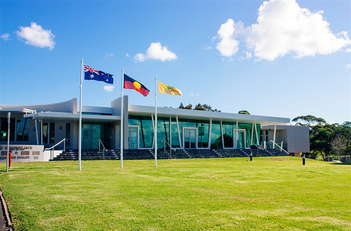 Grassed area with three flag poles in front of single storey Ulladulla Civic Centre