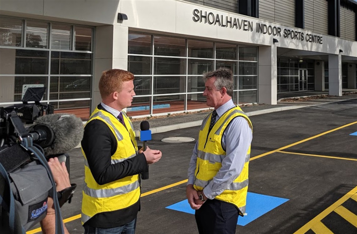 News reporter with microphone interviewing man in front of Shoalhaven Indoor Sports Centre