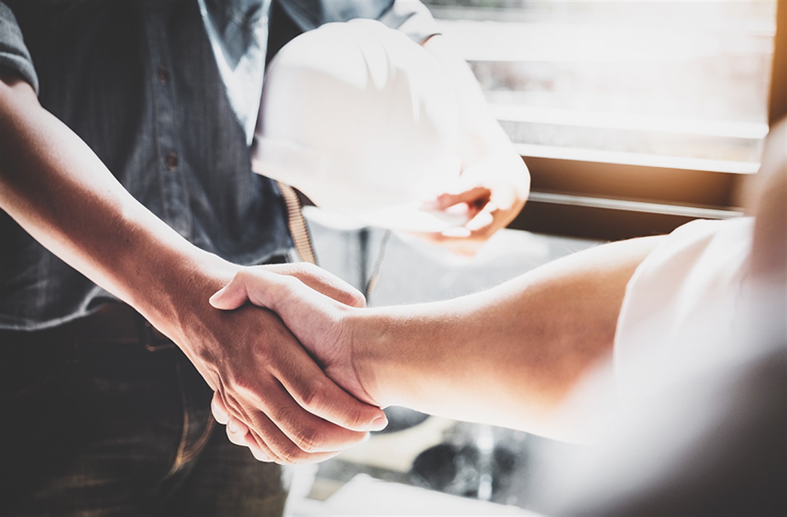Close up of a person with hardhat under their arm shaking hands with another person