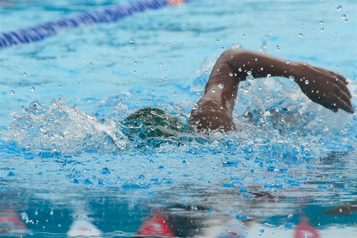 Close up of person in swimming cap mid freestyle stroke in olympic pool